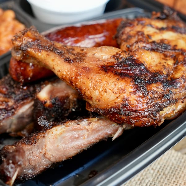 Close-up of Tony's Seafood's grilled chicken, ribs, and sausage in a black takeout container.